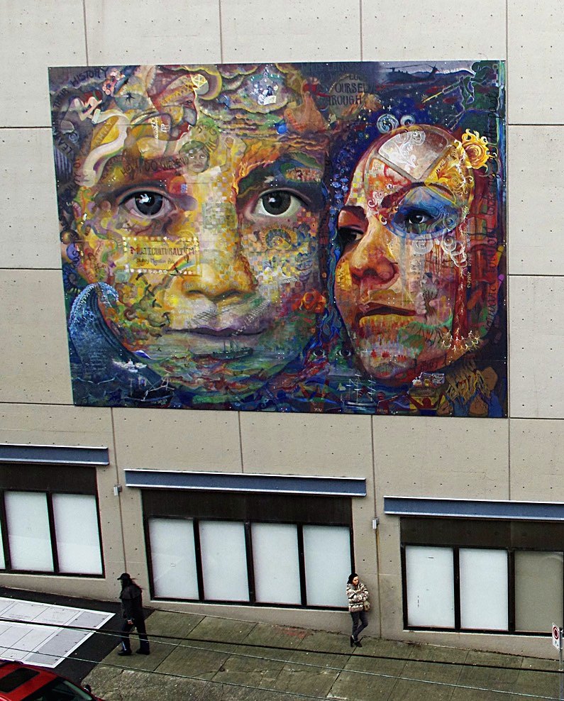 The Belonging Action mural, two large faces built from many smaller marks, installed high on the Harbour Centre facade in Vancouver