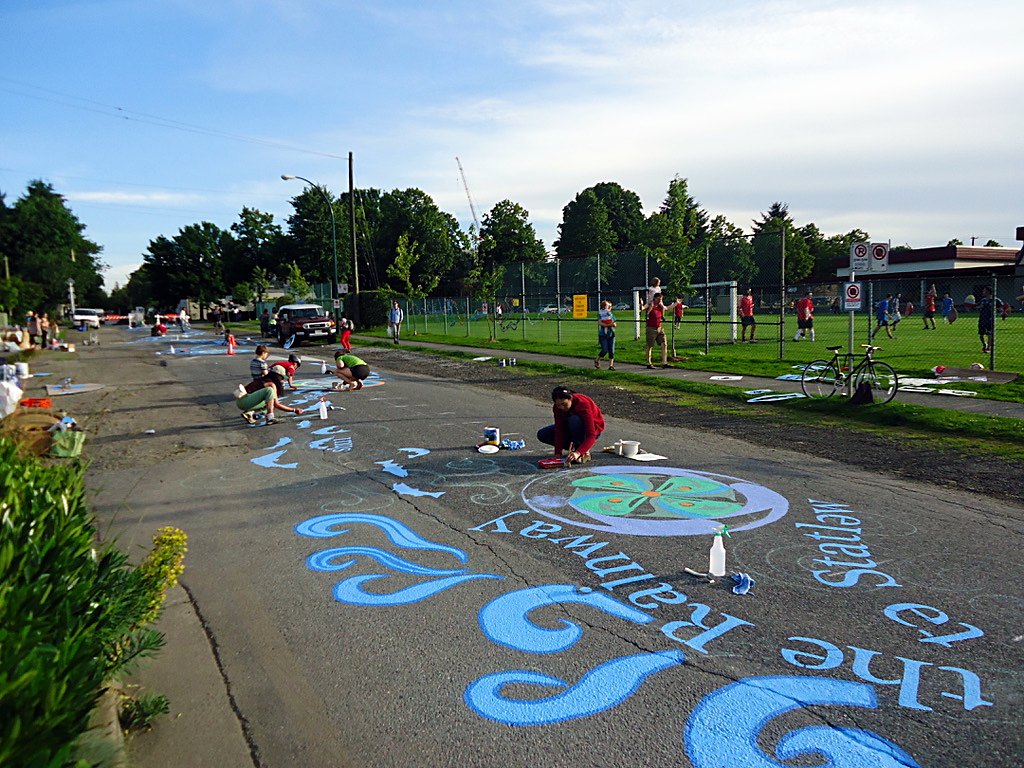 A water-themed street mural running the length of a city block, being painted by neighbours and local businesses