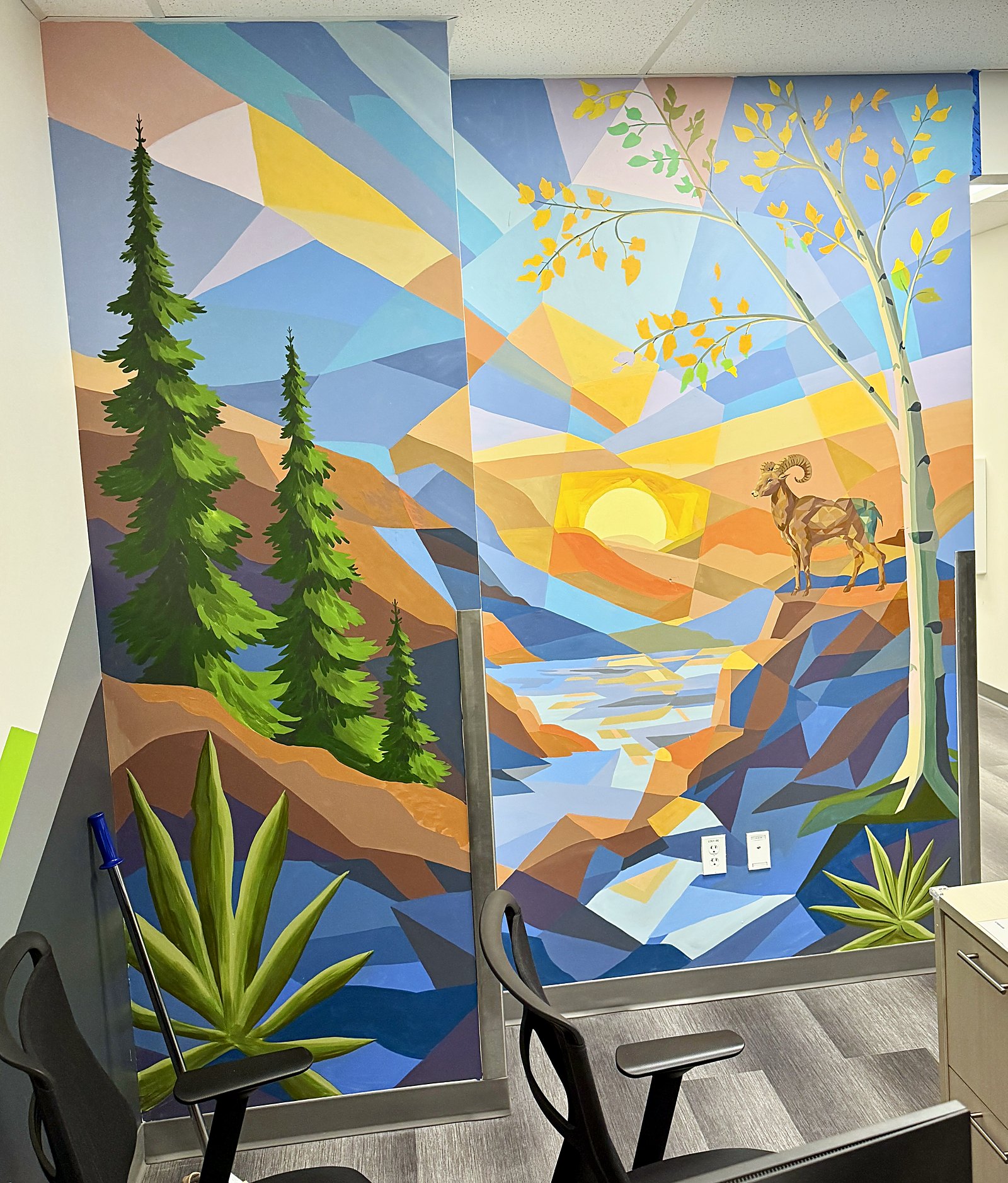 A mural behind the wellness center counter, a faceted mountain landscape with a stream and ram built around dodecahedral geometry