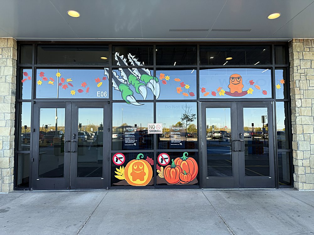 Hand-painted seasonal window display on the entrance glazing of an Amazon fulfillment center in Colorado, october 2025. harvest and halloween across the entrance doors