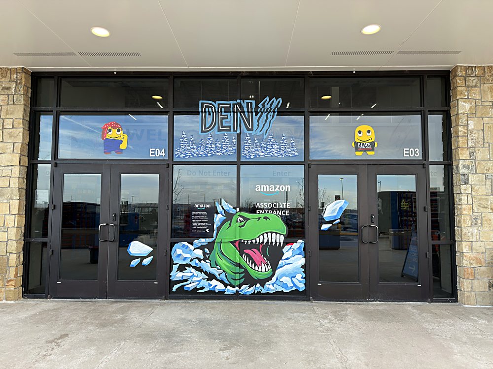 Hand-painted seasonal window display on the entrance glazing of an Amazon fulfillment center in Colorado, february 2026. the site code lettered in ice