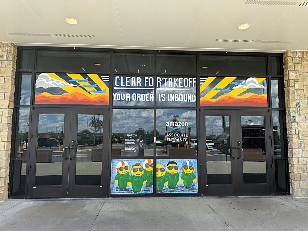 Hand-painted seasonal window display on the entrance glazing of an Amazon fulfillment center in Colorado, may 2026. clear for takeoff, the prime week theme