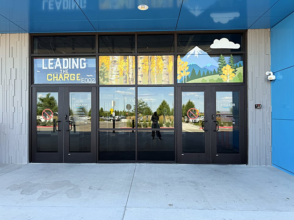 Hand-painted seasonal window display on the entrance glazing of an Amazon fulfillment center in Colorado, july 2026. leading the charge, summer landscape