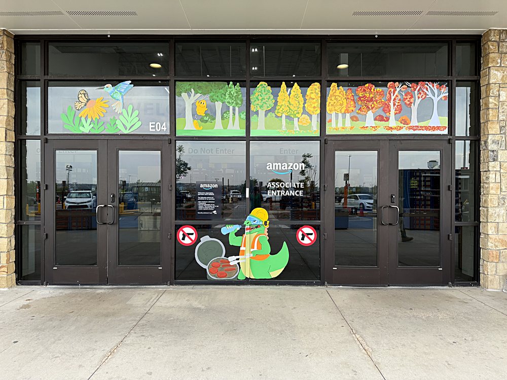 Hand-painted seasonal window display on the entrance glazing of an Amazon fulfillment center in Colorado, august 2026. forest panels running the width of the glass