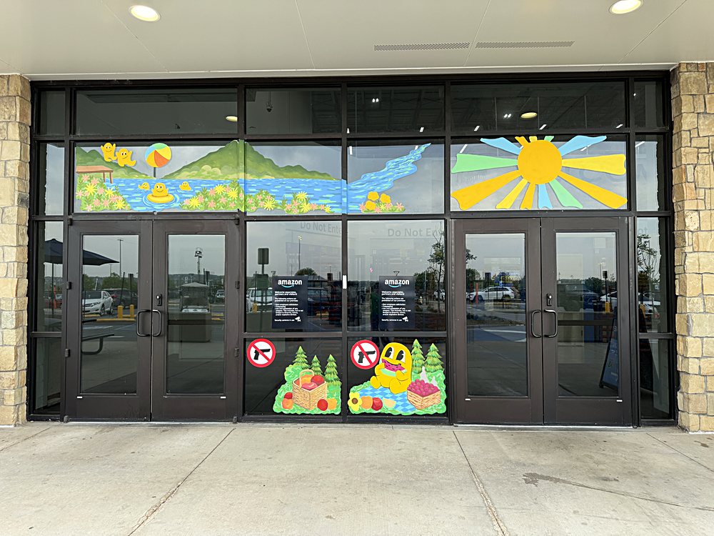 Hand-painted seasonal window display on the entrance glazing of an Amazon fulfillment center in Colorado, august 2026. sunrise over the treeline